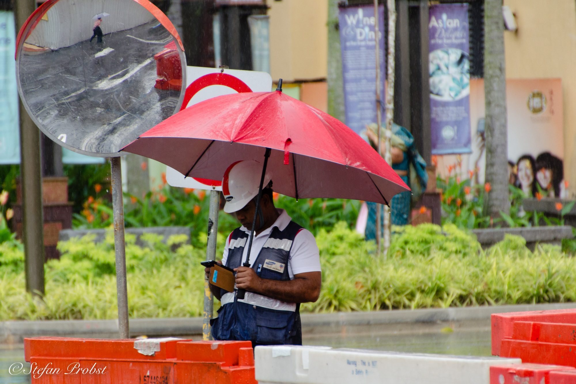 Bauarbeiter mit Regenschirm und Smartphone in den Straßen Singapurs