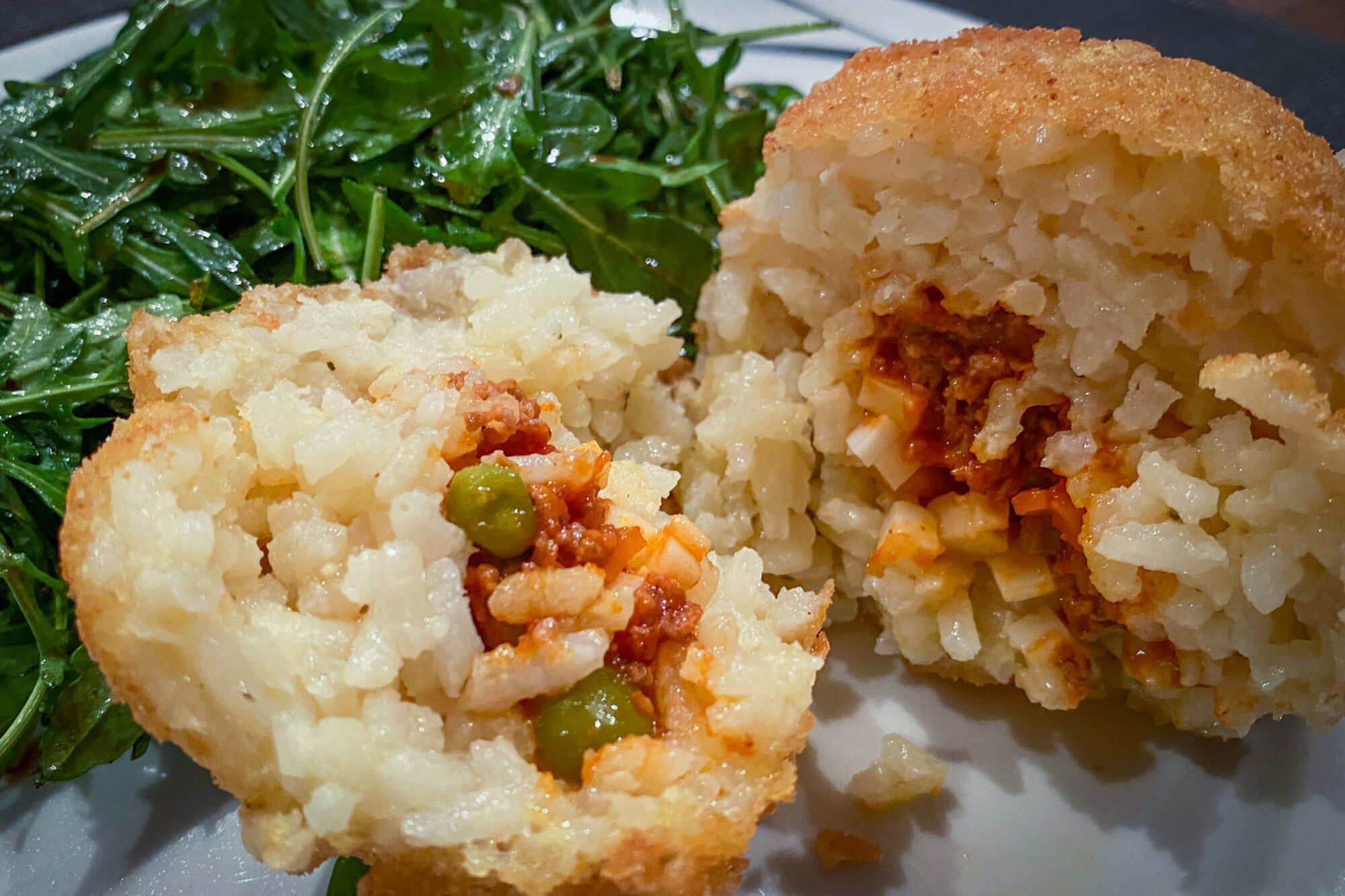 Arancini aufgeschnitten und angerichtet mit Rucolasalat